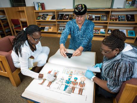 Three people looking at book in library