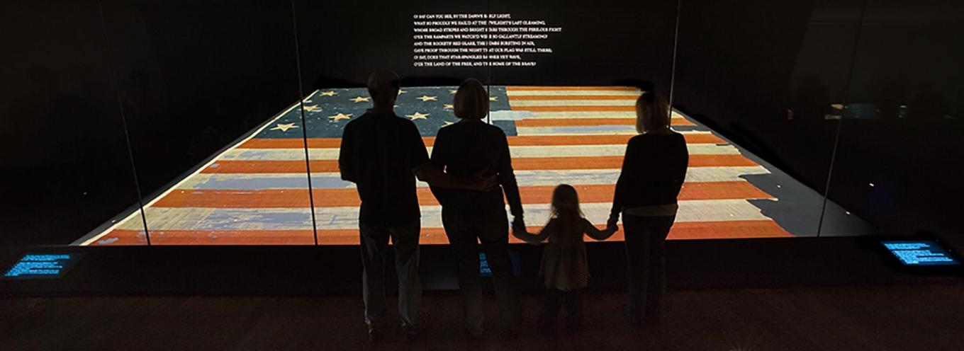 Family in front of the Star-Spangled Banner exhibit which features the American flag and the song lyrics